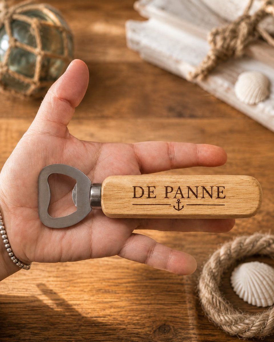 Houten flesopener met metalen opener-kop, gegraveerd met 'DE PANNE' en een anker, vastgehouden in een hand